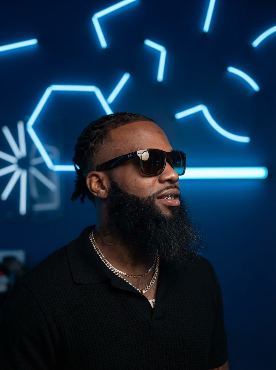 Delano in sunglasses, black knit polo and layered chains, tight three-quarter profile, kept exactly as photographed